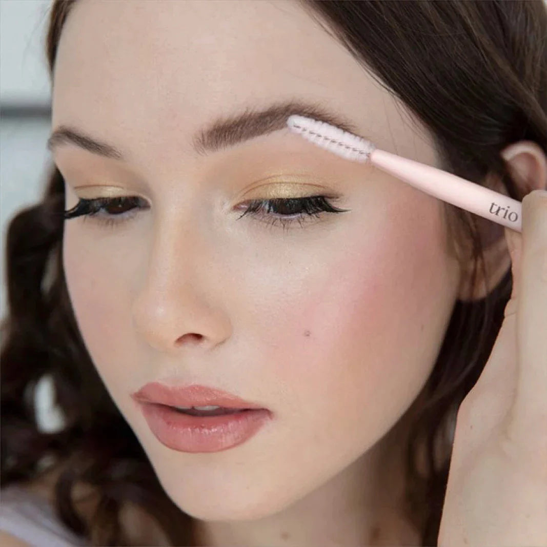 woman using the brow trio stamp stencil kit, coming her brows with a spoolie
